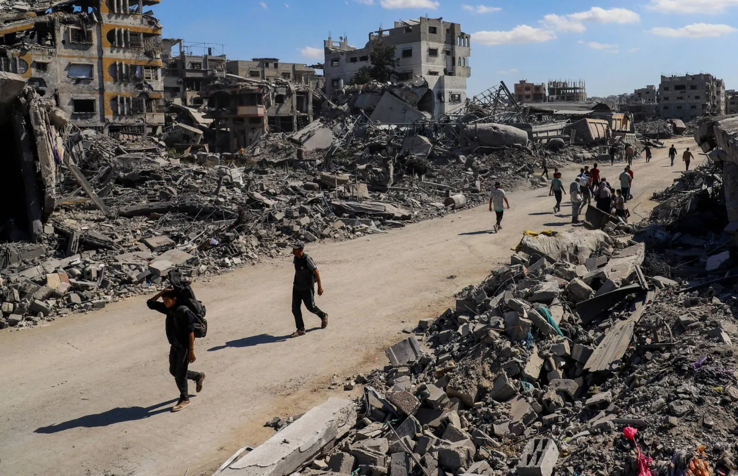 Palestinians walk past the rubble of destroyed buildings, amid a ceasefire between Israel and Hamas, in Gaza City, October 14, 2025. REUTERS/Ebrahim Hajjaj