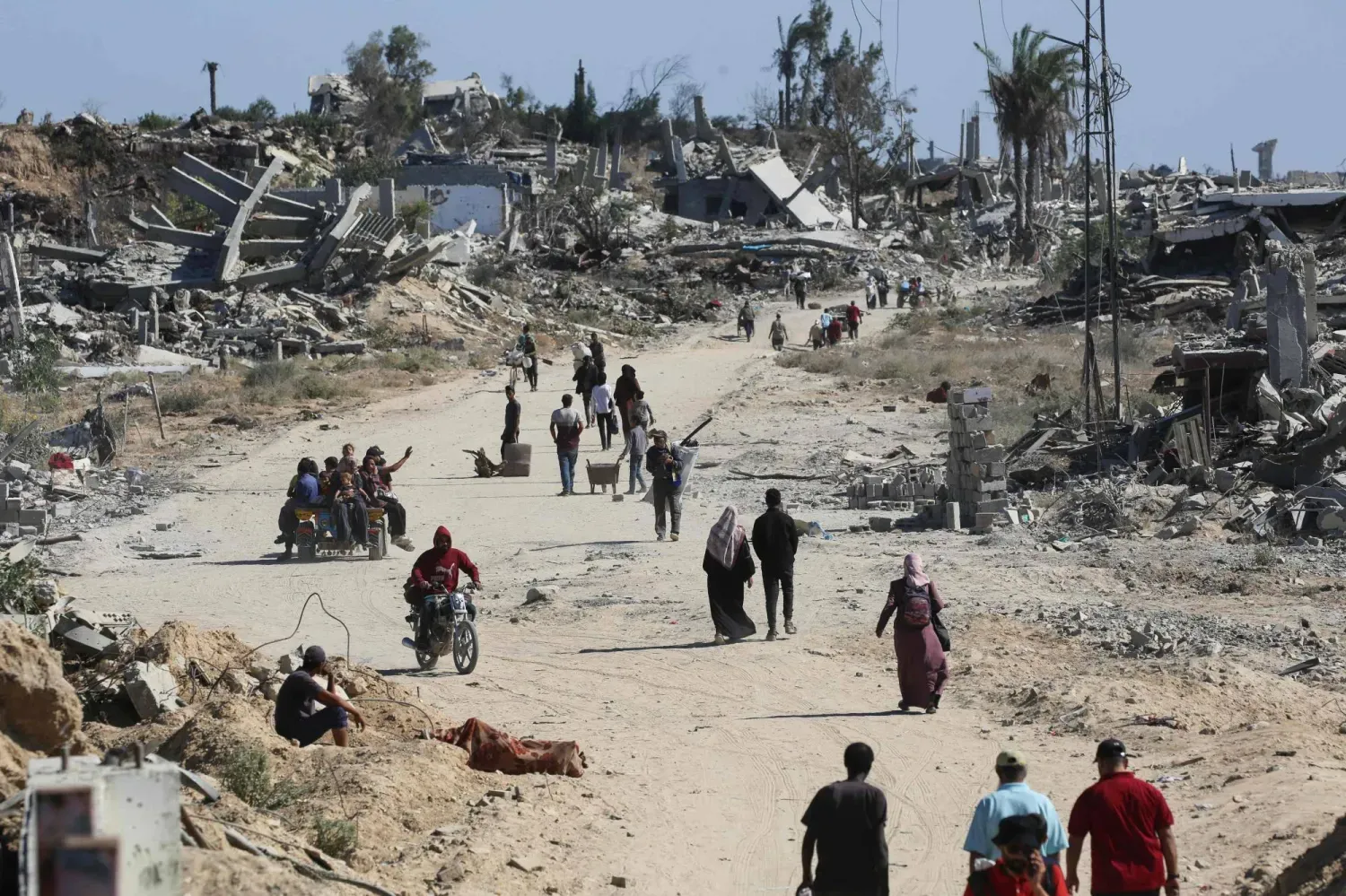 Yerinden edilmiş Filistinliler, Gazze Şeridi'nin merkezindeki Nuseyrat mülteci kampının kuzeyindeki evlerine dönerken yıkılmış binaların yanından geçiyorlar (AFP)