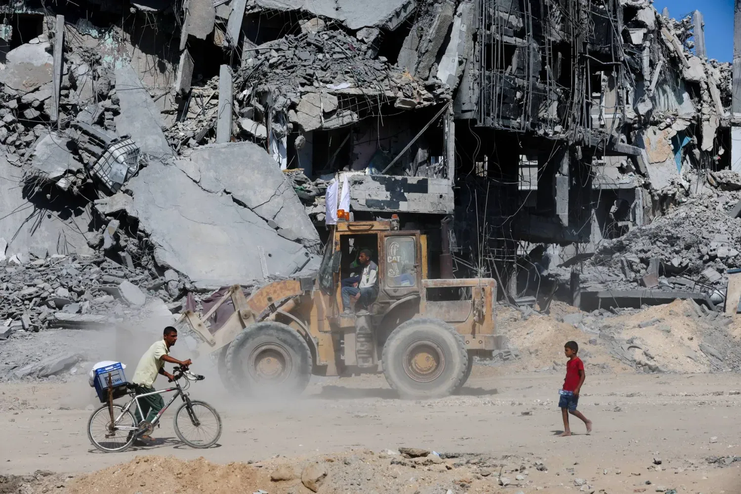 Savaşın sona ermesinin ardından dün Gazze'nin güneyindeki Han Yunus'ta enkazların önünden geçen Filistinliler (Reuters)