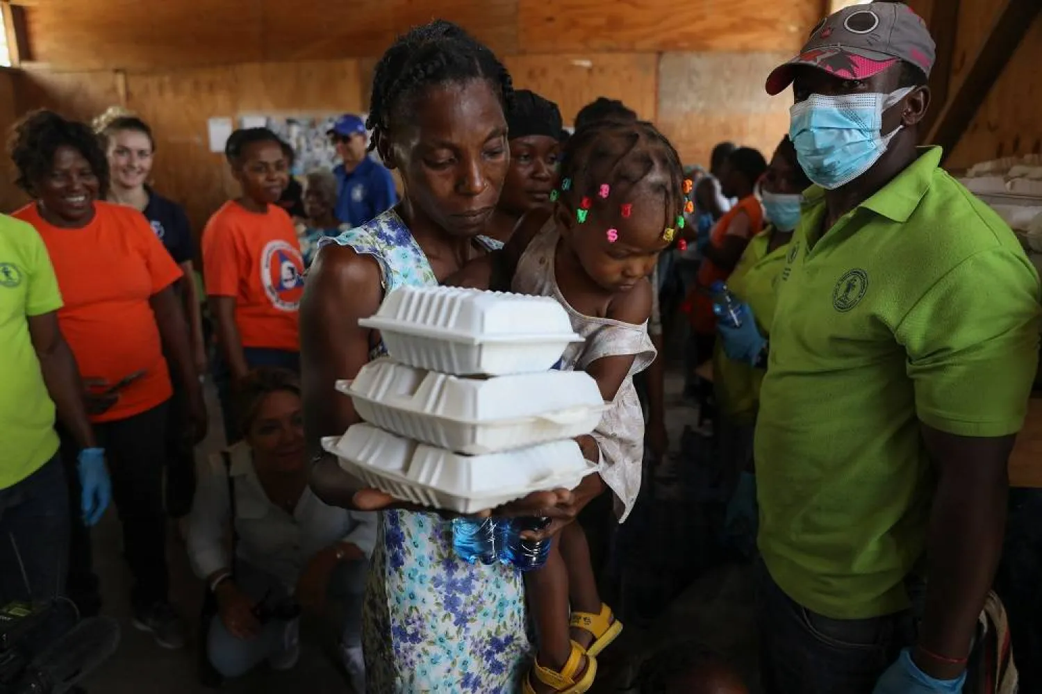 A woman carrying a child walks away with food from the World Food Program (WFP) at the Jean Marie Vincent High School whish has been turned into a shelter for families displaced by gang violence in the Tabarre neighborhood of Port-au-Prince, Haiti, Thursday, July 25, 2024. (AP)