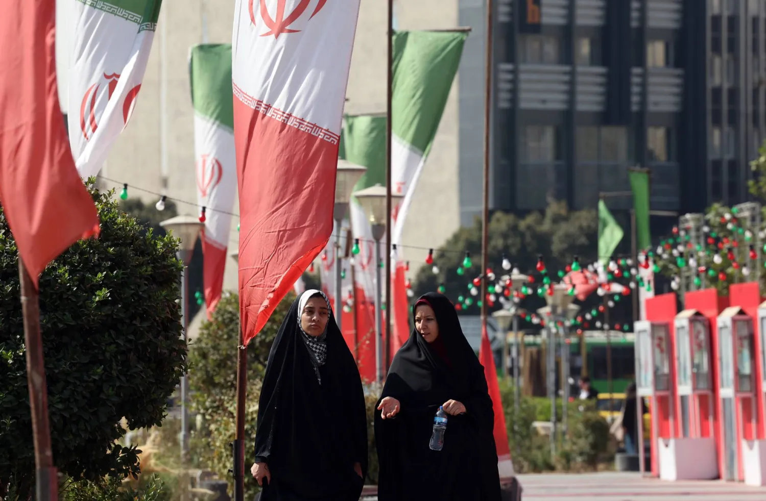  Veiled Iranian women walk past Iran's national flags on a street in Tehran, Iran, 13 October 2025. (EPA)