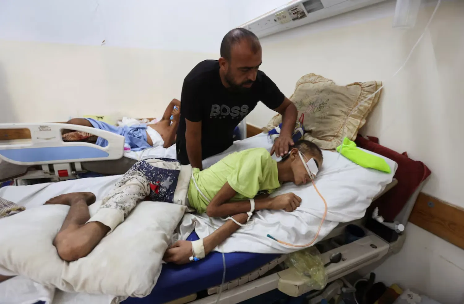 Injured Palestinian Hassan Qlob, 18, who his father says was shot in the head more than two months ago while out seeking food, lies on a bed as he waits for the Rafah crossing to reopen so he can receive treatment abroad, as his father Ibrahim tends to him, after a ceasefire between Israel and Hamas in Gaza went into effect, at Nasser Hospital in Khan Younis, southern Gaza Strip October 15, 2025. REUTERS