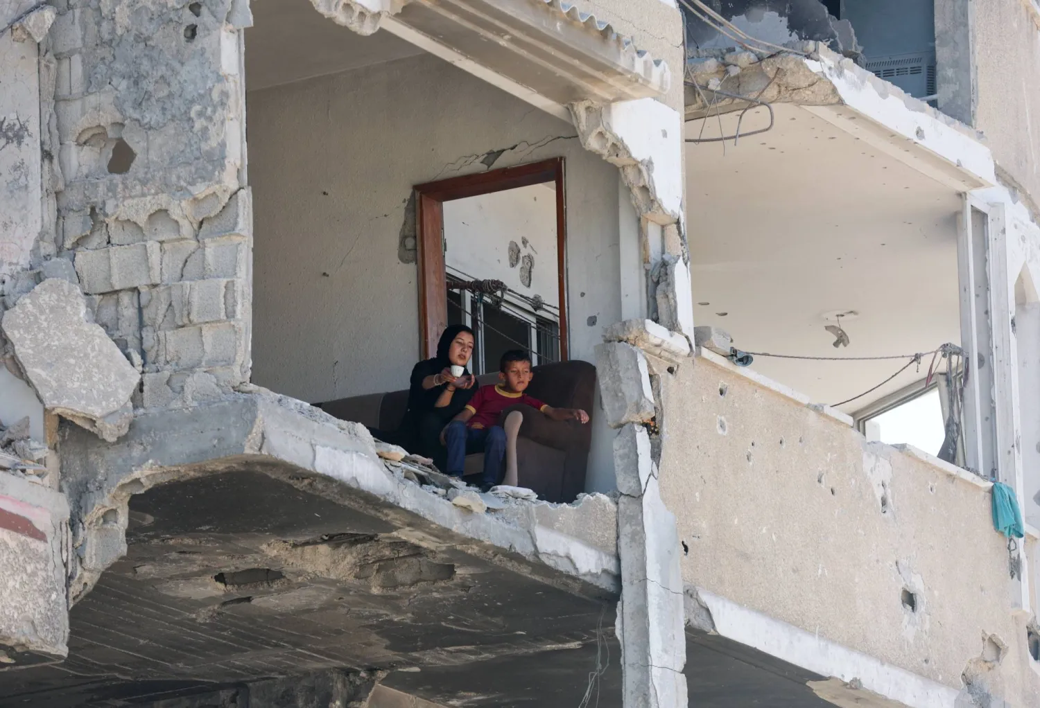 فلسطينيون يجلسون على حافة منزل متضرر من الحرب في خان يونس بجنوب قطاع غزة (رويترز)