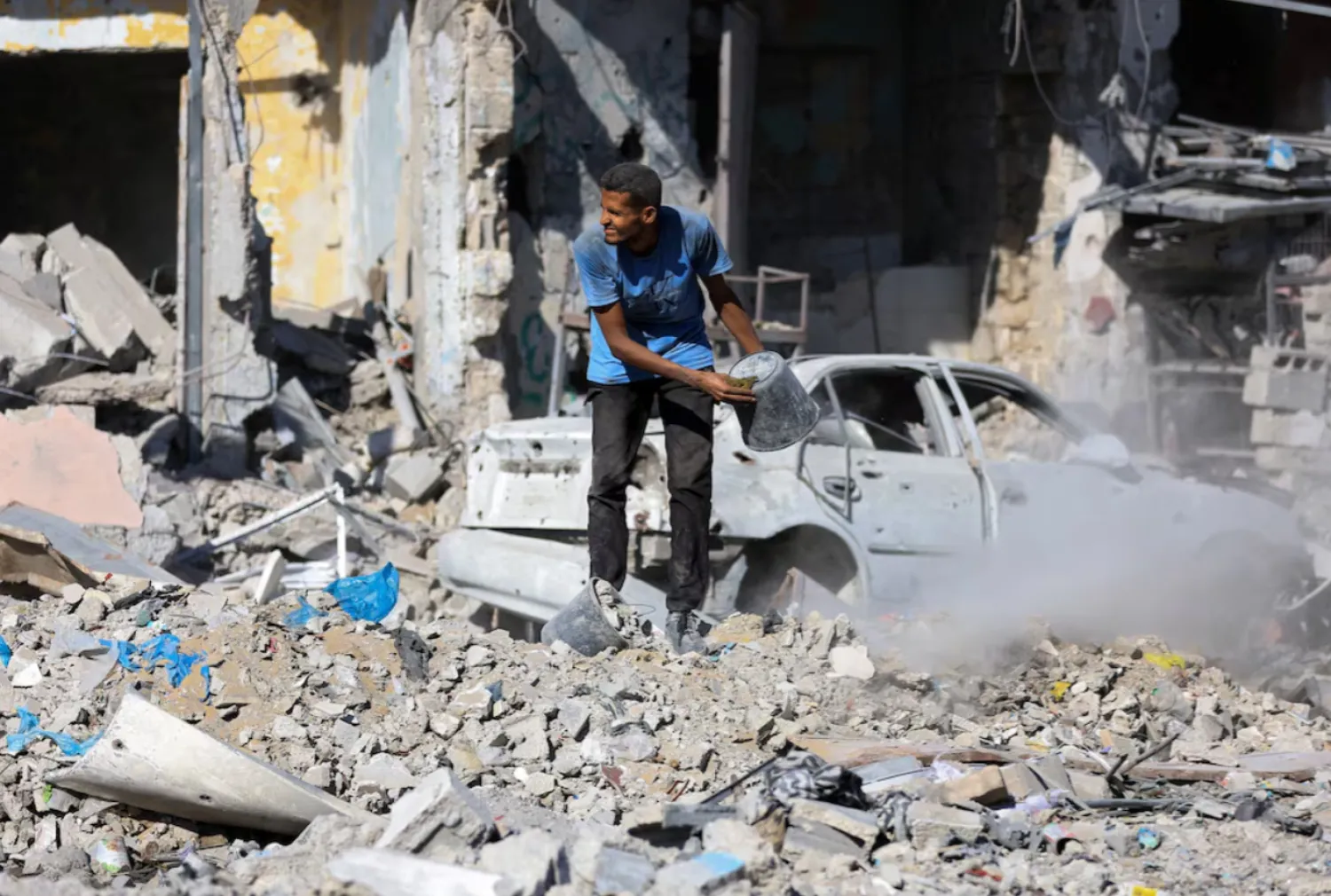 A Palestinian man holds a bucket as he stands among rubble, amid a ceasefire between Israel and Hamas, in Gaza City, October 14, 2025. REUTERS/Dawoud Abu Alkas