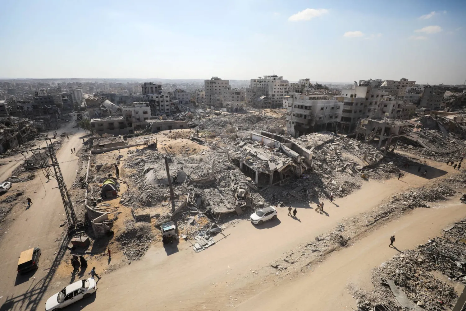 فلسطينيون يسيرون بين أنقاض مبان مدمرة في مدينة غزة أمس (رويترز)