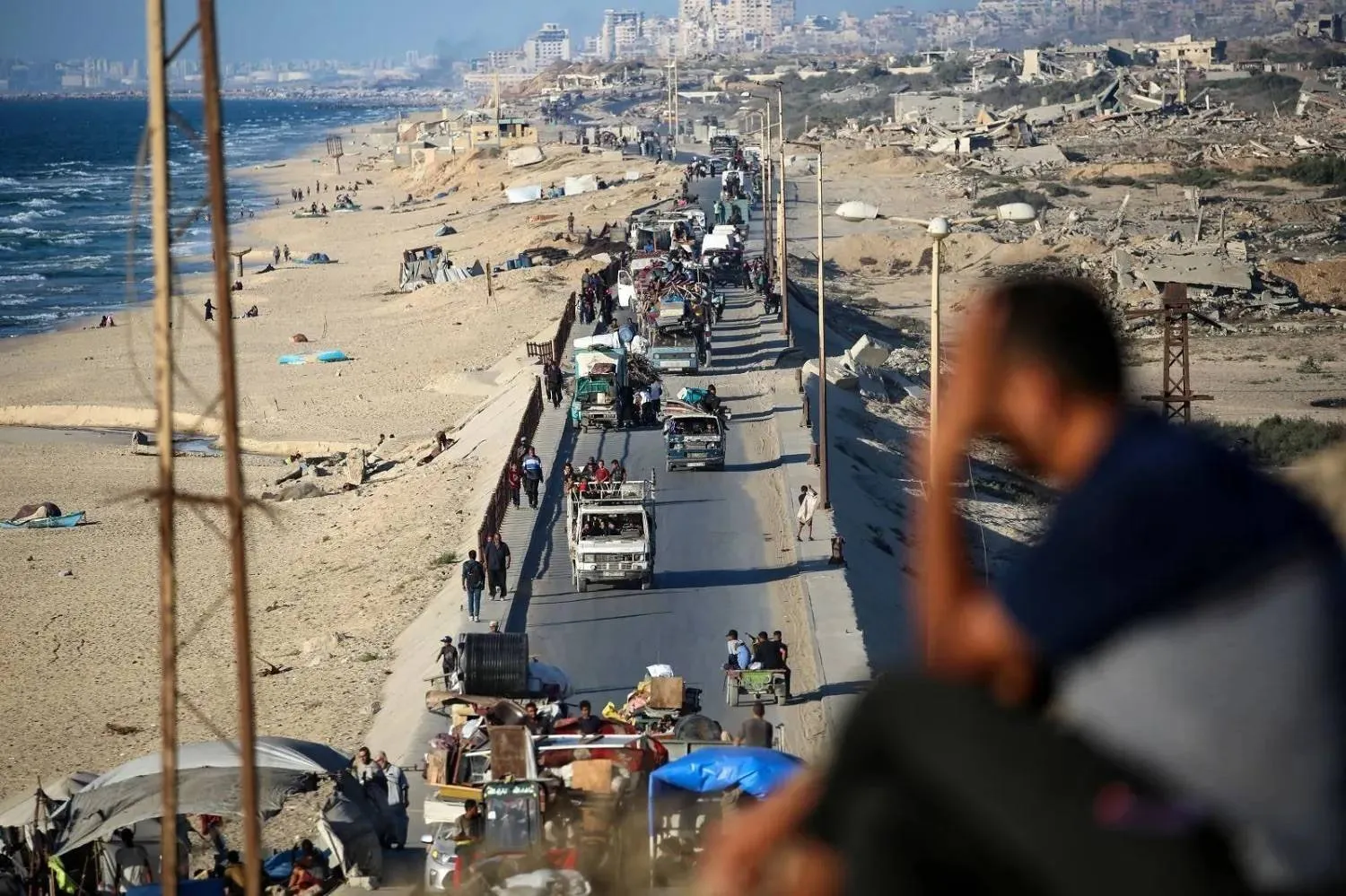 A man watches Palestinians fleeing south from Gaza City with their belongings along the coastal road (AFP)