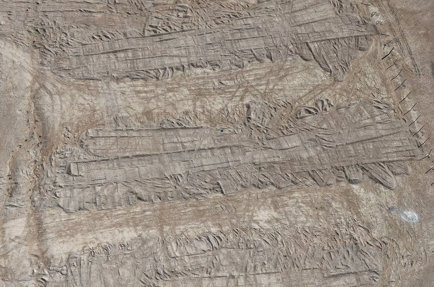 A drone view of imprints, made by bulldozer tracks, on the soil covering a burial trench of a mass grave in the eastern Syrian desert near the town of Dhumair, February 27, 2025. REUTERS/Khalil Ashawi
