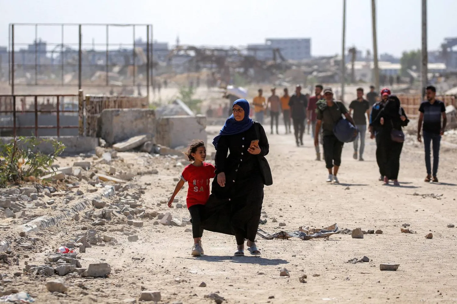 امرأة تسير مع فتاة في طريقها إلى مدينة غزة عبر ما يُسمى ممر نتساريم من النصيرات (أ.ف.ب)