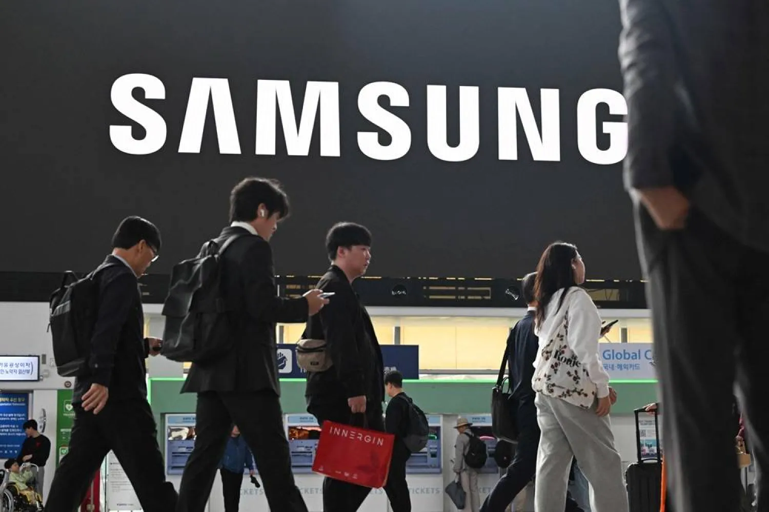 People walk past a large electronic screen showing the Samsung logo at Seoul train station in Seoul on October 14, 2025. (AFP)