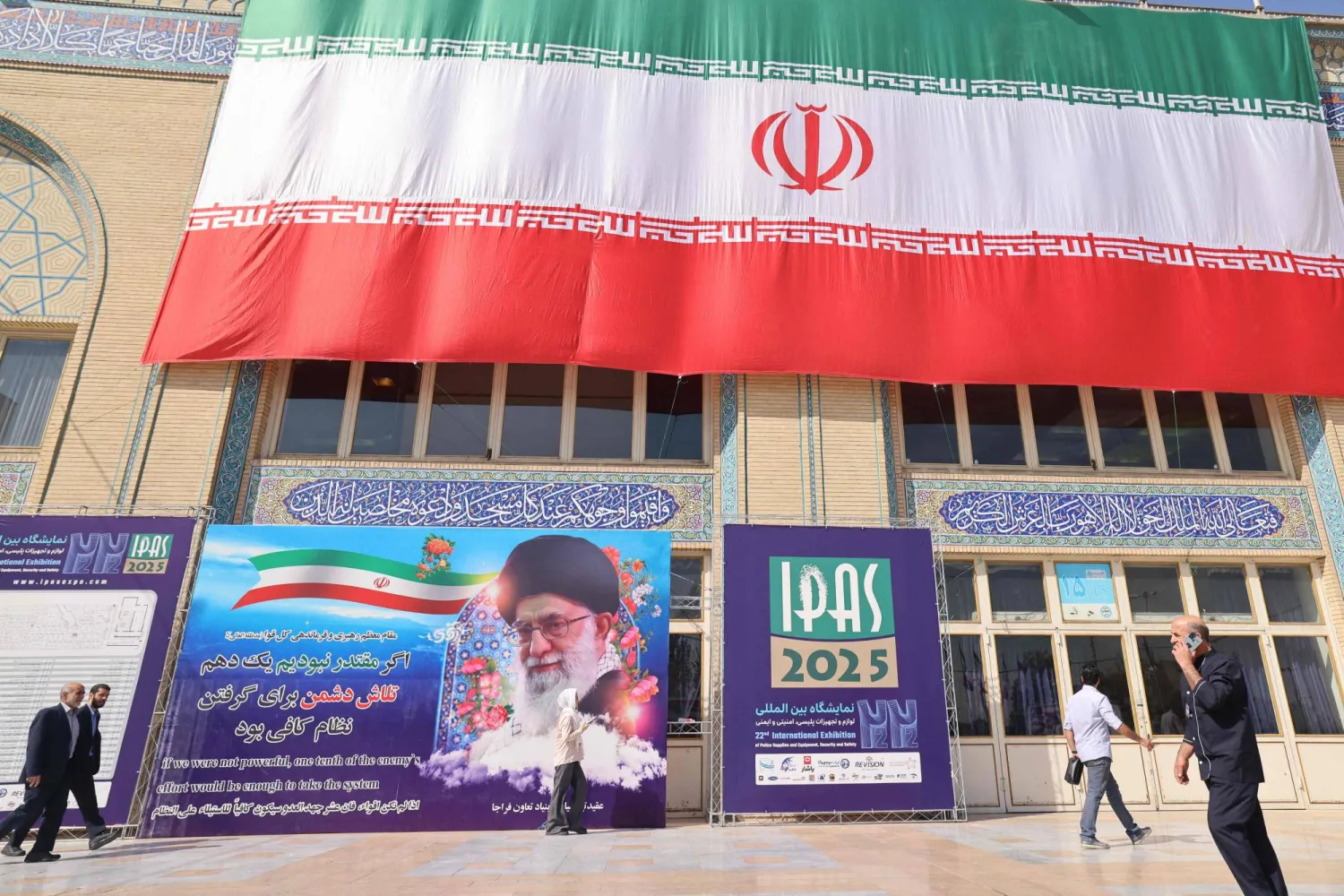  Iranians walk past a poster featuring Iran's Supreme Leader Ali Khamenei outside the venue of the 22nd Police and Security Equipment Exhibition at Imam Khomeini Mosque in Tehran on October 15, 2025. (AFP) 