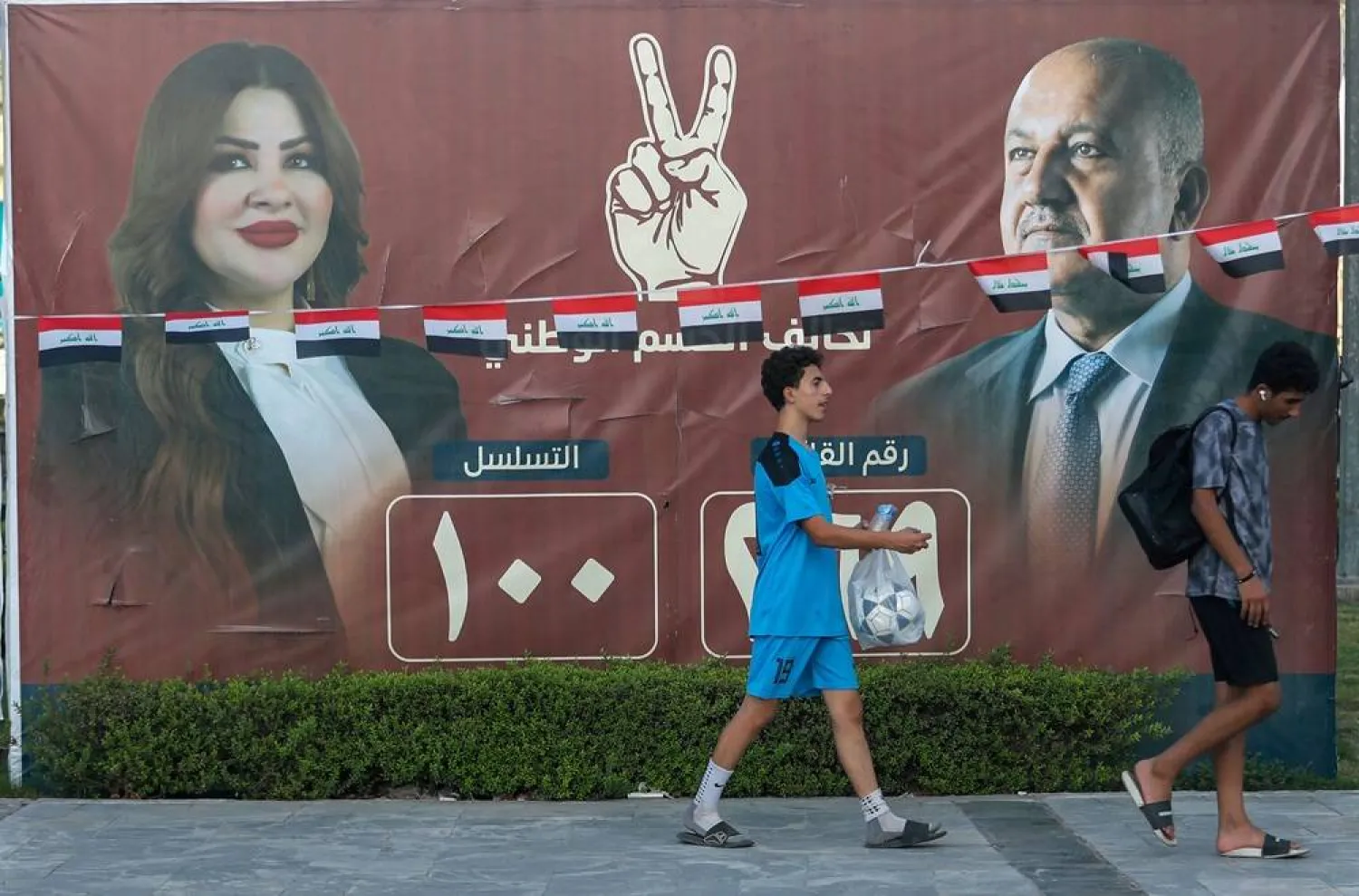 People walk past electoral billboards on a street in Baghdad on October 14, 2025, ahead of parliamentary elections on November 11. (AFP)