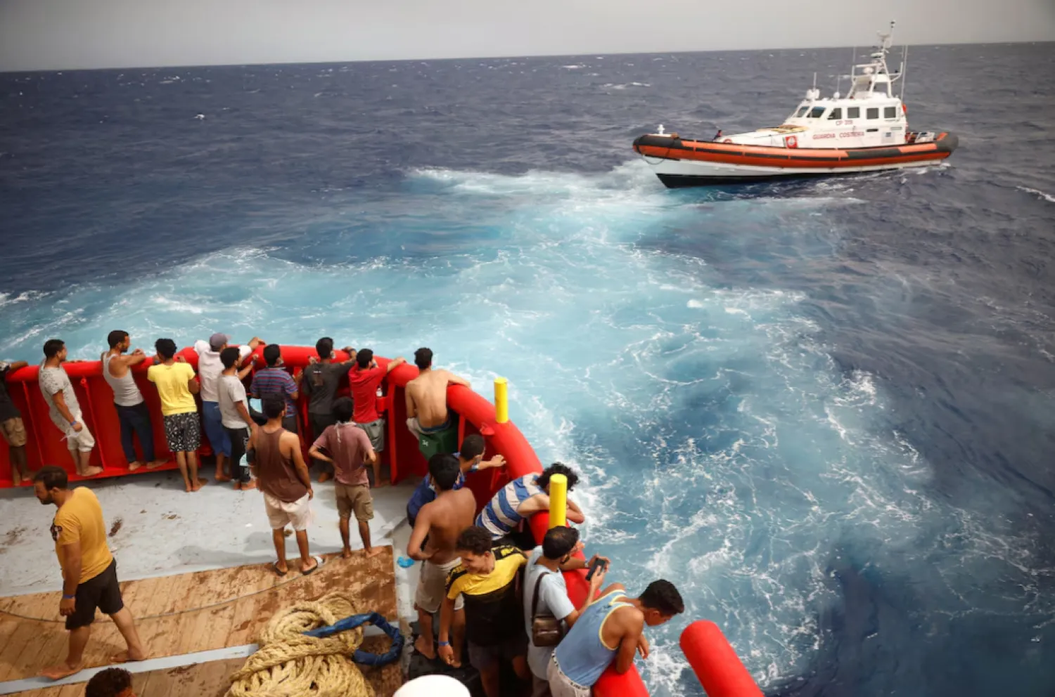 Migrants on board of NGO Proactiva Open Arms Uno rescue boat looks at boat Guardia Costiera heading to Lampedusa island, in central Mediterranean Sea, close to Lampedusa island, Italy, August 19, 2022. REUTERS/Juan Medina/File Photo