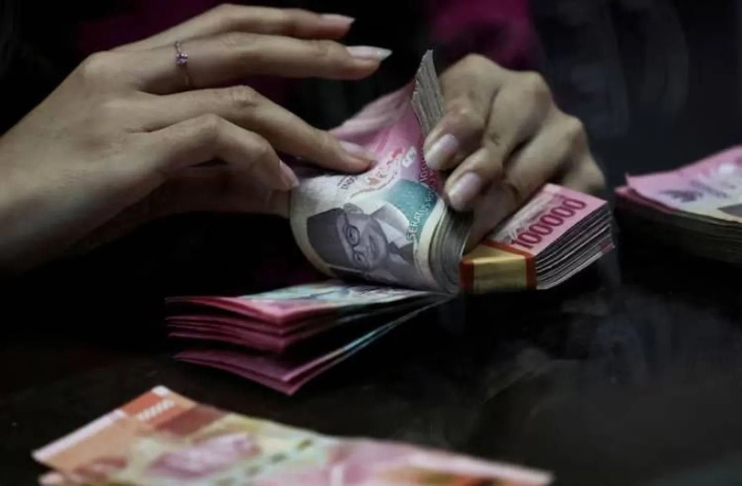 أحد الصرافين يعد أوراق نقدية بالروبية في محل صرافة في جاكرتا (رويترز)