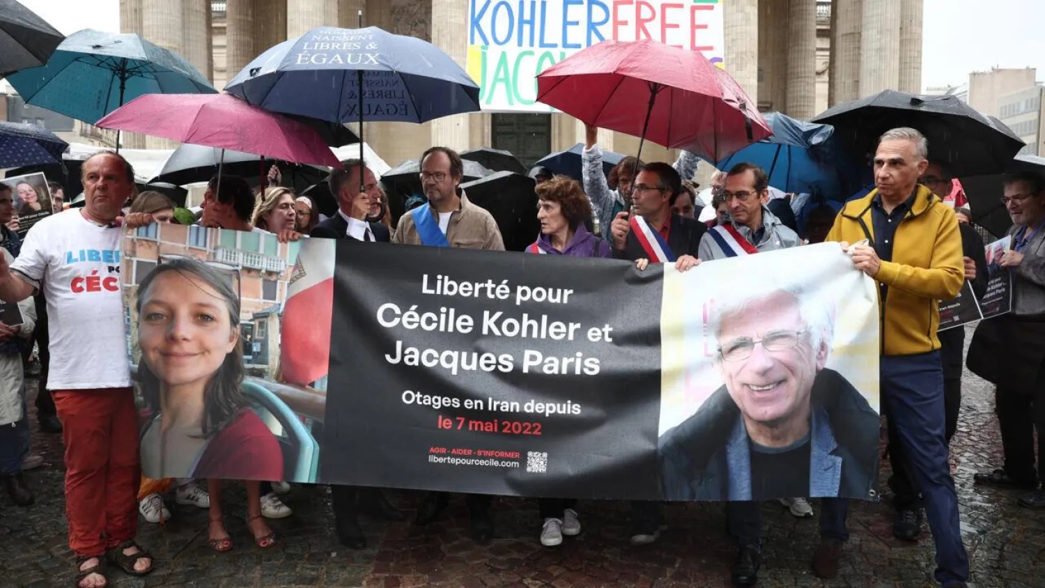 Relatives and supporters pose behind a banner with the portrait of Cecile Kohler (L) and Jacaues Paris (R) who are being held in Iran since May 2022 on espionage charges, in Paris, on July 6, 2025. Sebastien Dupuy, AFP
