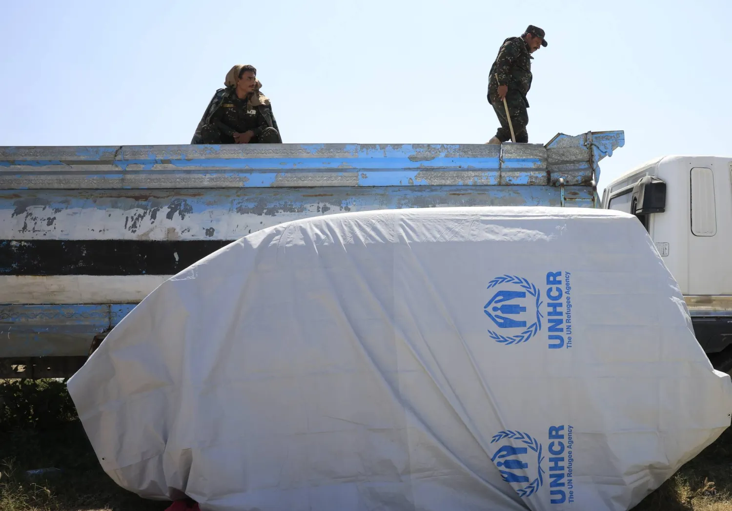 عناصر حوثيون في صنعاء قرب غطاء بلاستيكي يحمل شعار المفوضية السامية للأمم المتحدة لشؤون اللاجئين (إ.ب.أ)