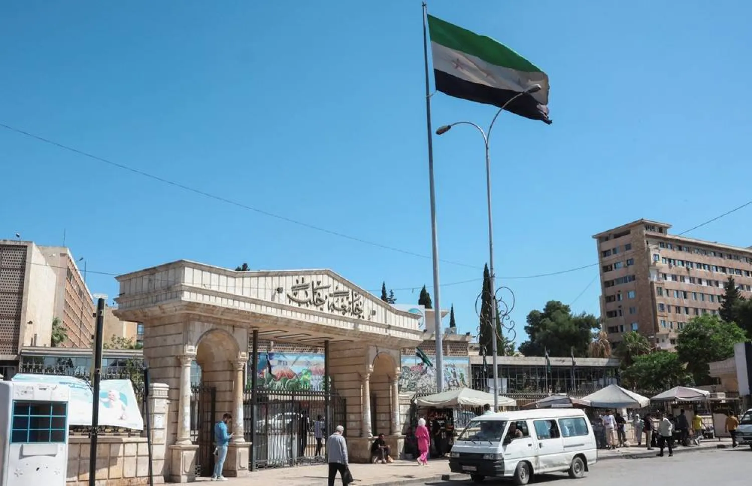 People walk near the Syrian flag, as US President Donald Trump announced that he would order the lifting of sanctions on Syria, in Aleppo, Syria May 14, 2025. (Reuters)