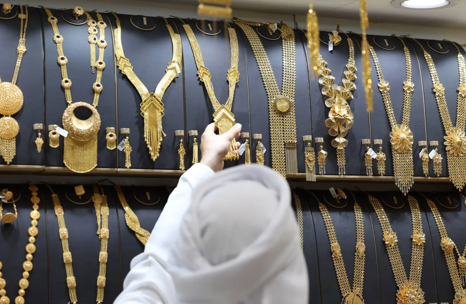 عارِض يعرض قطعة من الذهب على أحد الزبائن بمتجر مجوهرات داخل سوق الذهب في دبي (إ.ب.أ)