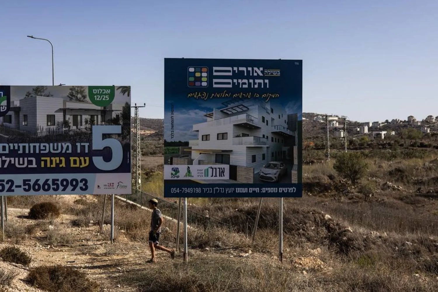 An Israeli settler walks between billboards advertising homes ahead of the return of freed hostage Avinatan Or in the Israeli settlement of Shiloh in the occupied West Bank on October 21, 2025. (AFP) 