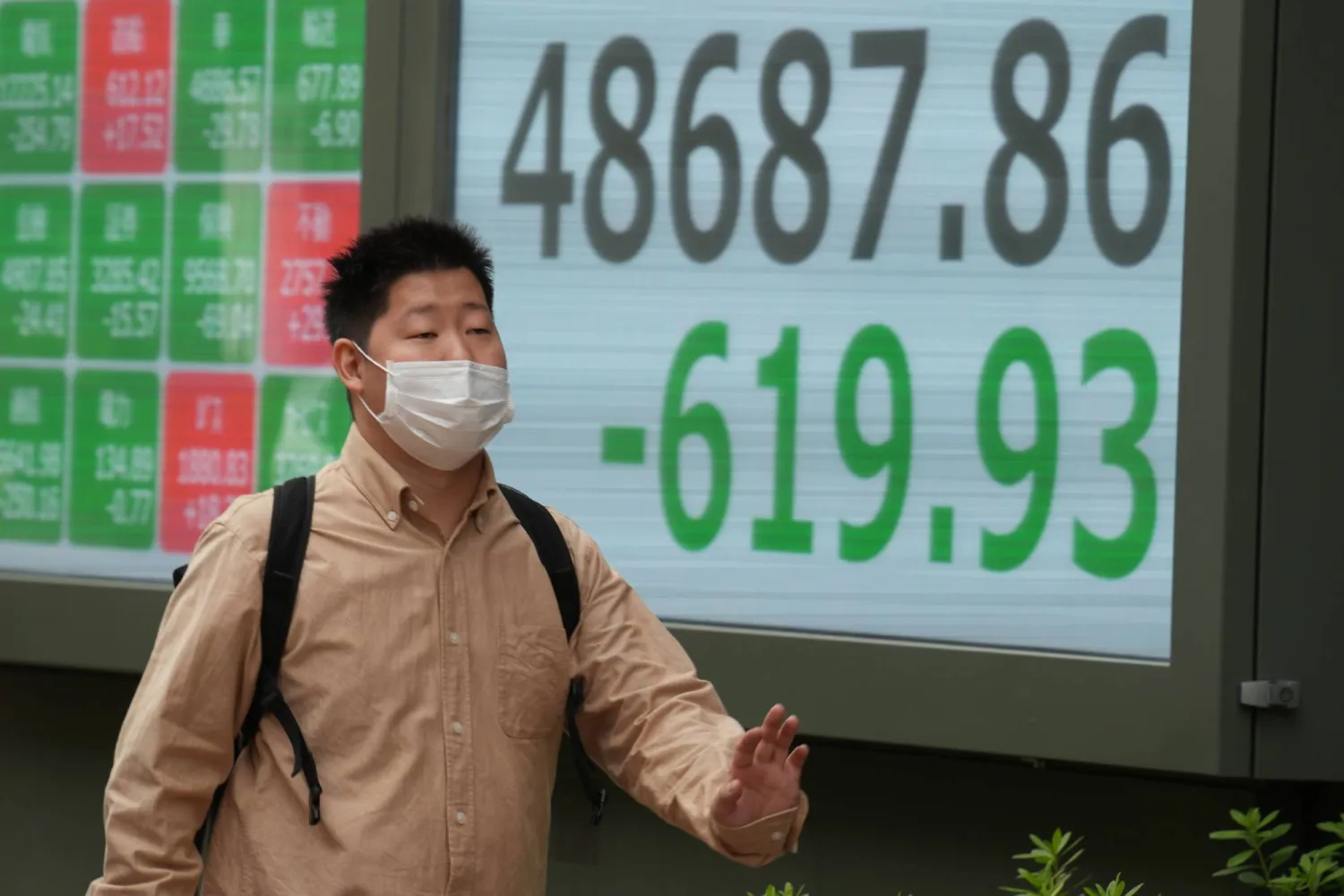 أحد المشاة يمر أمام لوحة إلكترونية تعرض حركة الأسهم في وسط العاصمة اليابانية طوكيو (أ.ب)