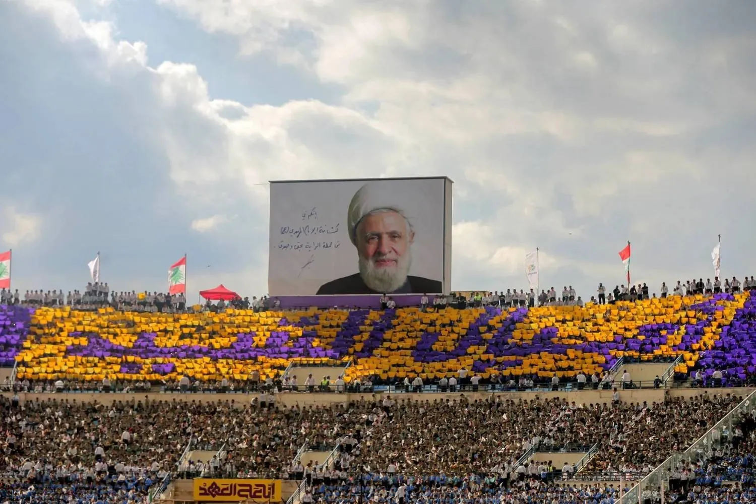 12 October 2025, Lebanon, Beirut: Pro-Iranian Hezbollah al-Mahdi Scouts raise colored cards to form the words "Generation of the Martyr" under a picture of Hezbollah Secretary General Naim Qassem during a ceremony at Beirut Sports City to mark the first anniversary of assassinated party leader Hassan Nasrallah death by Israeli attack on Lebanon. Photo: Marwan Naamani/dpa