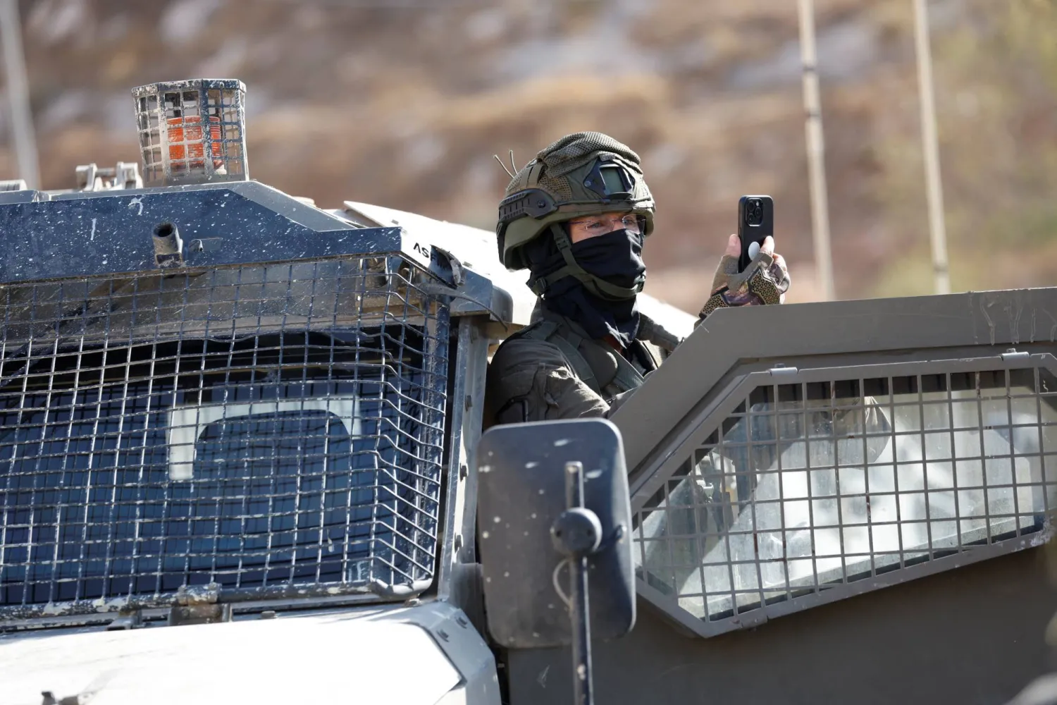 A member of the Israeli force uses a mobile phone as Israeli forces block the access of Palestinians and foreign activists to olive trees during the olive harvest, near Hebron, in the Israeli-occupied West Bank, October 23, 2025. REUTERS/Mussa Qawasma