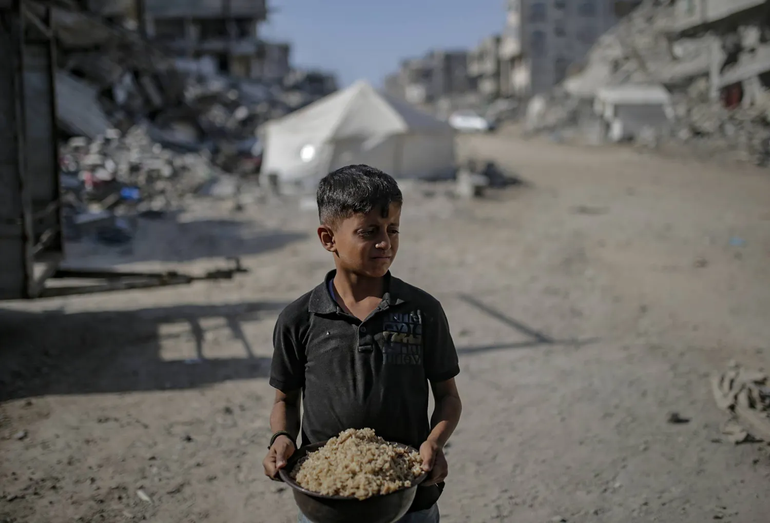 طفل فلسطيني يحمل وعاء من الأرز حصل عليه من تكية خيرية في مدينة غزة (إ.ب.أ)