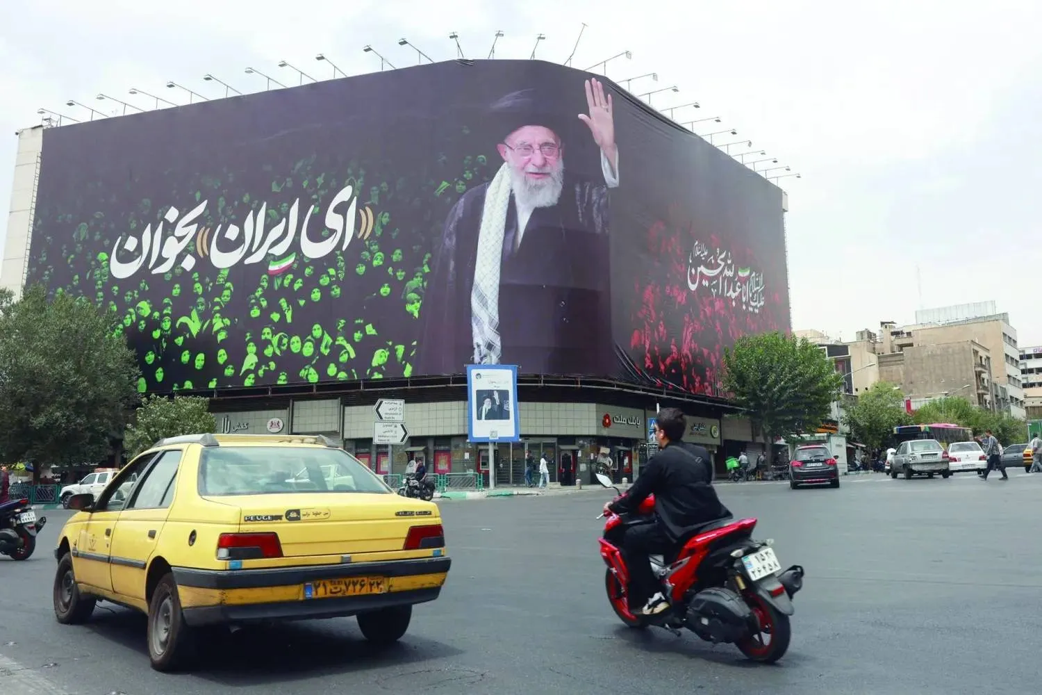 Cars pass a billboard of Khamenei reading “O Iran” at Enghelab (Revolution) Square in central Tehran (AFP)
