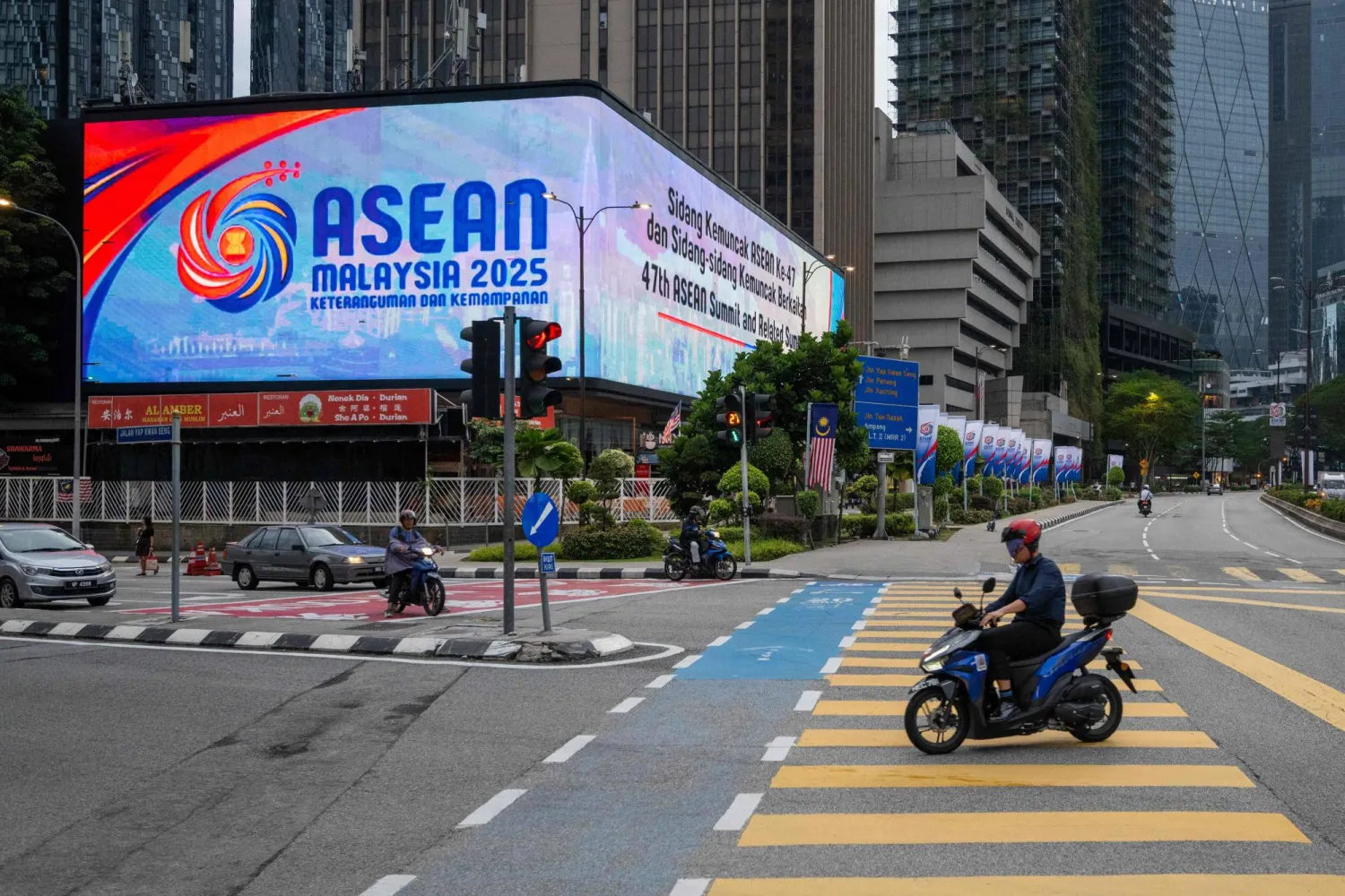 A man rides his motorcycle past a big screen showing the logo of the Association of Southeast Asian Nations (ASEAN) in front of Malaysia's Petronas Twin Towers ahead of the 47th ASEAN Summit in Kuala Lumpur on October 23, 2025. (Photo by Mohd RASFAN / AFP)