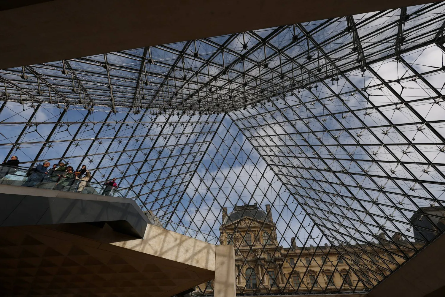 زوار يتجولون أسفل الهرم الزجاجي في متحف اللوفر (رويترز)