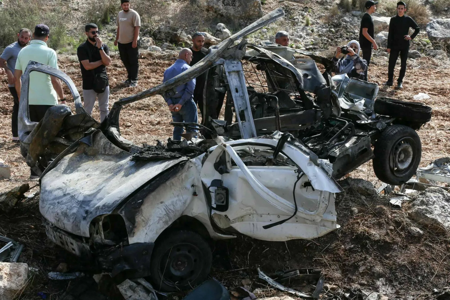أشخاص يتفقدون حطام سيارة استهدفتها غارة إسرائيلية في قرية حاروف جنوب لبنان (أ.ف.ب)