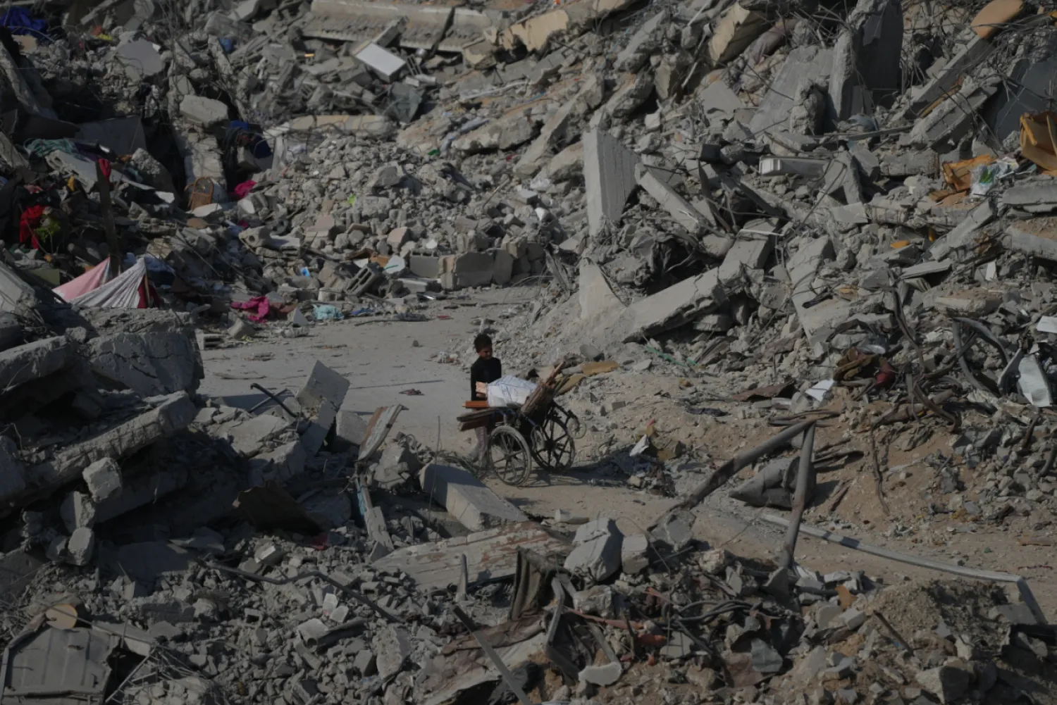 A boy pushes a wheelchair through the rubble of buildings destroyed in the war between Israel and Hamas, in the al-Nafaq area of the Sheikh Radwan neighborhood in Gaza City, Friday, Oct. 24, 2025. (AP Photo/Abdel Kareem Hana)