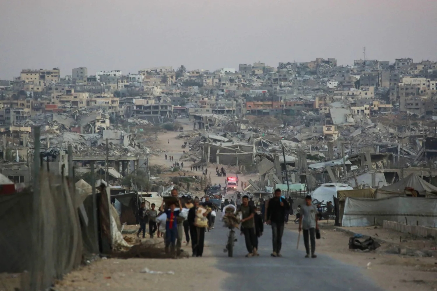 فلسطينيون يمشون على طول طريق وسط المباني المدمرة في خان يونس (أ.ف.ب)