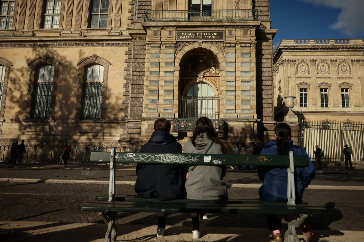 أشخاص يجلسون لمشاهدة الواجهة والنافذة التي دخل منها اللصوص إلى متحف اللوفر يوم الأحد الماضي (أ.ب)