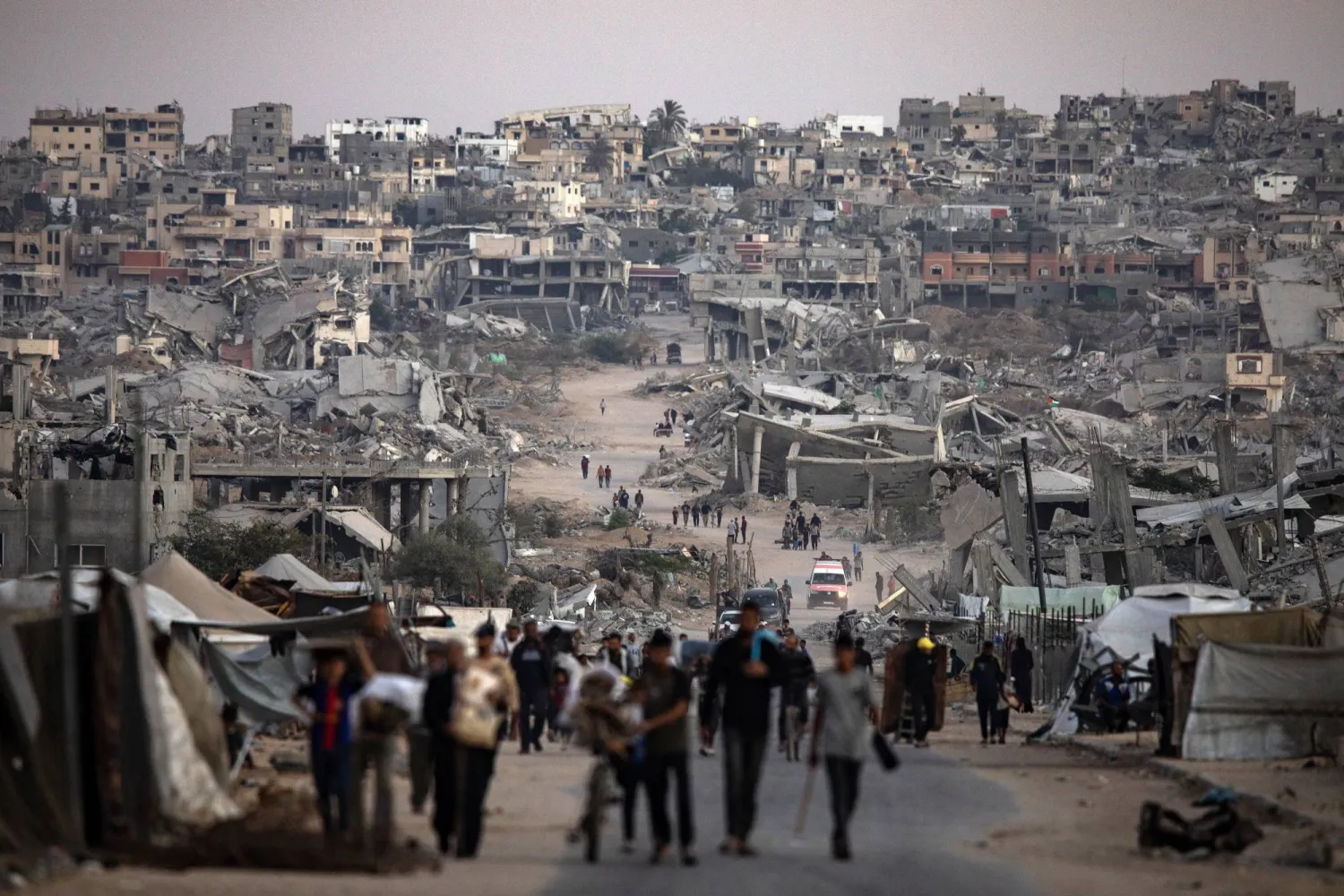 فلسطينيون يسيرون وسط المباني المدمرة في خان يونس بجنوب قطاع غزة (إ.ب.أ)