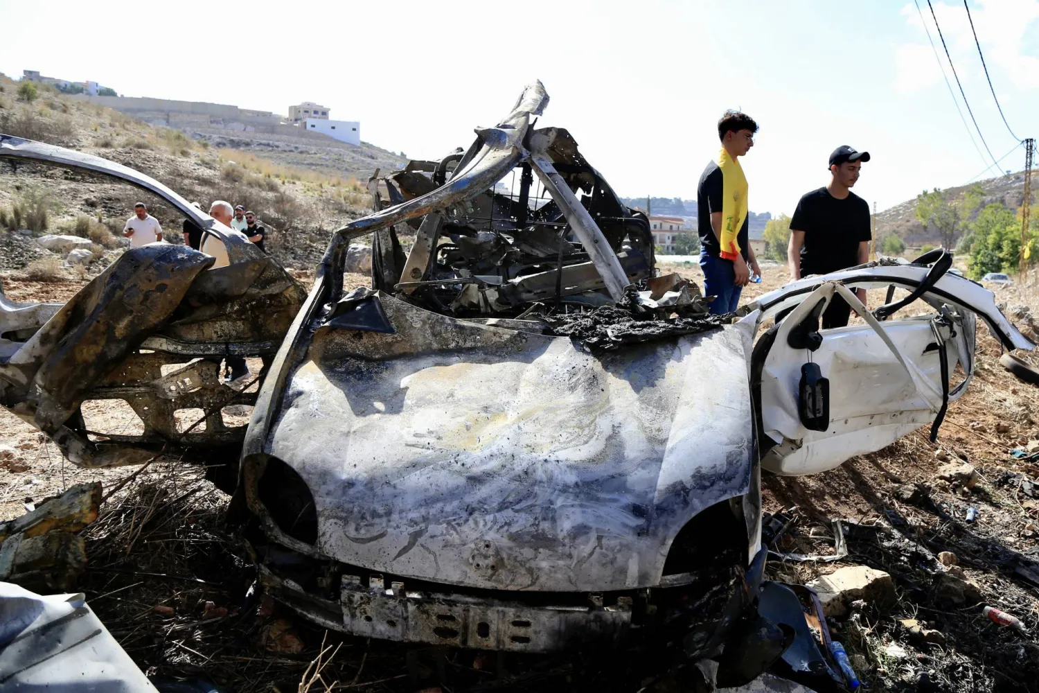 أشخاص يتفقدون حطام سيارة استهدفتها طائرة مسيّرة إسرائيلية في قرية حاروف في محافظة النبطية جنوب لبنان - 25 أكتوبر 2025 (إ.ب.أ)