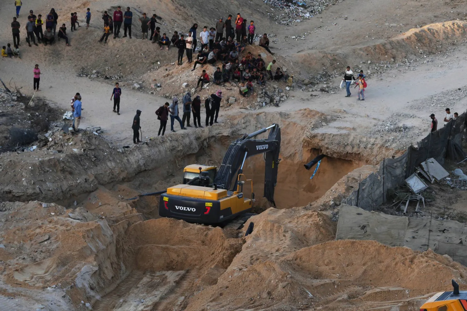 يُشاهد الفلسطينيون آليات وفرقاً من مصر خلال عمليات البحث عن جثث الرهائن بمدينة حمد في خان يونس جنوب قطاع غزة أمس (أ.ب)