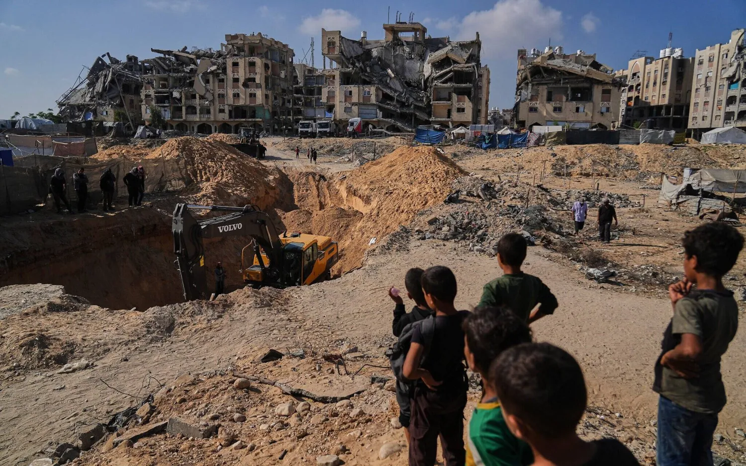 فلسطينيون يراقبون آلات وعمالاً مصريين خلال بحثهم عن جثث رهائن في مدينة حمد بخان يونس جنوب قطاع غزة 28 أكتوبر 2025 (أ.ب)