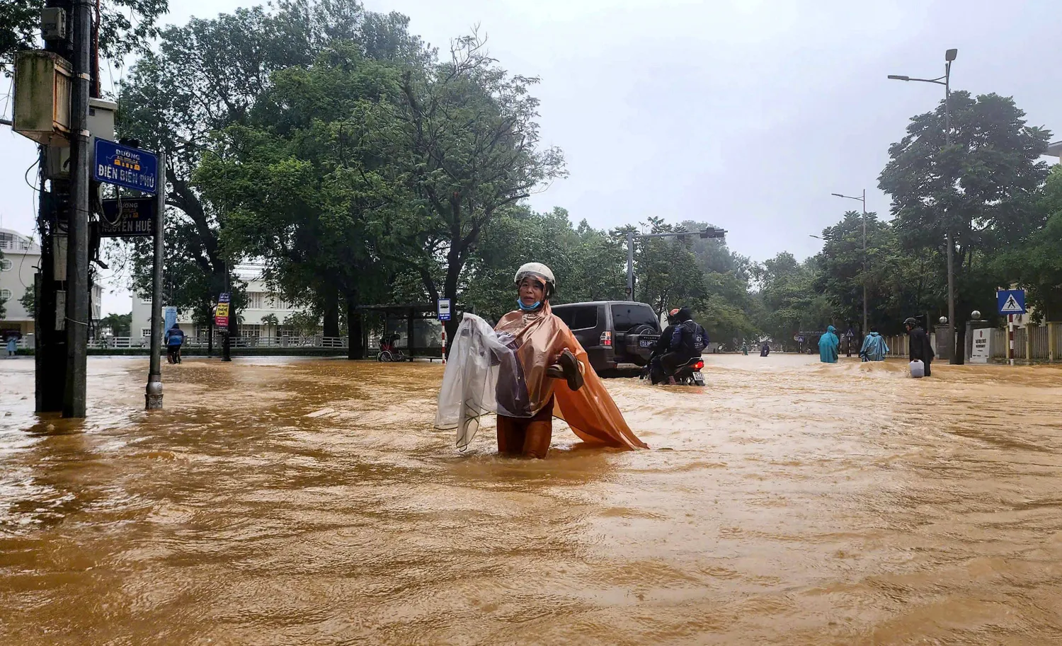 A woman wearing a raincoat wades through a flooded street in Hue on October 28, 2025. (Photo by AFP)