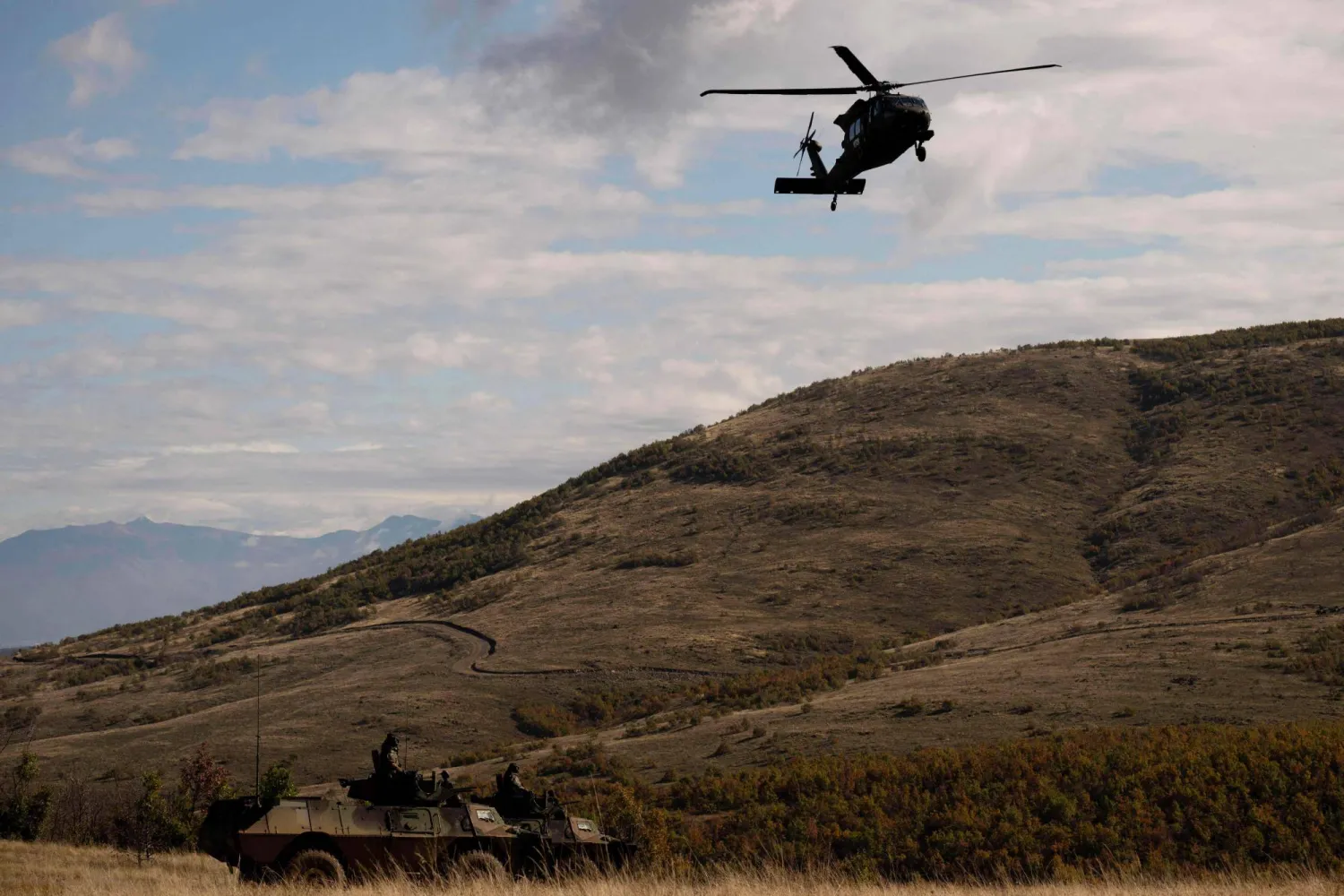 A NATO peacekeeping mission in Kosovo (KFOR) helicopter flies over armored vehicles of Kosovo Security Force (KSF) during the military exercise "Wolf Arrow" to validate the third regiment of land forces, in the village of Babaj Bokes, south-western Kosovo on October 28, 2025. (Photo by Armend NIMANI / AFP)