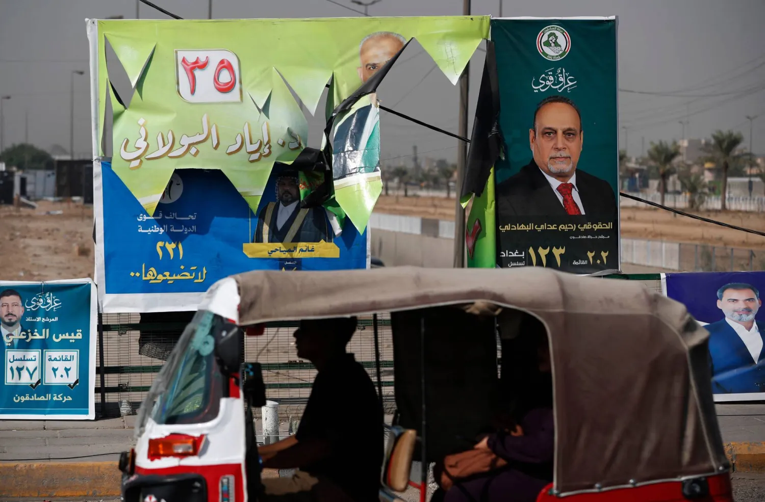 سيارة تمر أمام ملصقات انتخابية في مدينة الصدر شرق بغداد استعداداً للانتخابات البرلمانية (أ.ف.ب)