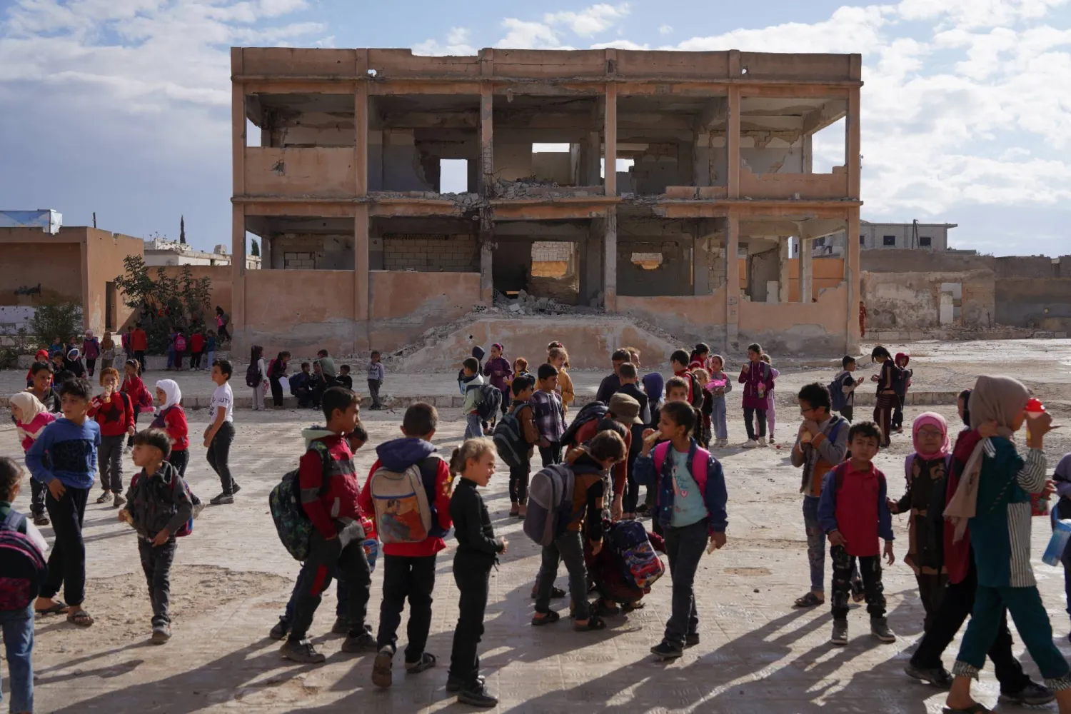 طلاب يتجمعون في ساحة مدرسة متضررة في ريف إدلب بسوريا في 9 أكتوبر 2025 (رويترز)