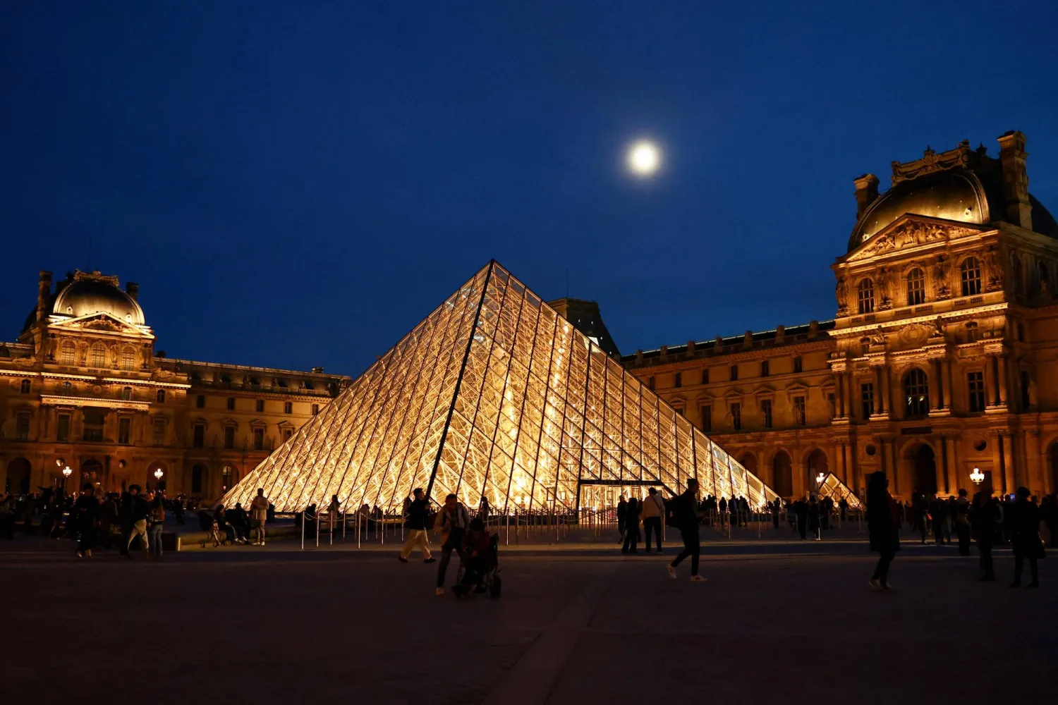 People walk near the glass Pyramid of the Louvre museum  as French police have arrested more suspects linked to the theft of treasures from the Louvre museum's Galerie d'Apollon (Apollo gallery), in Paris, France, October 30, 2025. (Reuters)