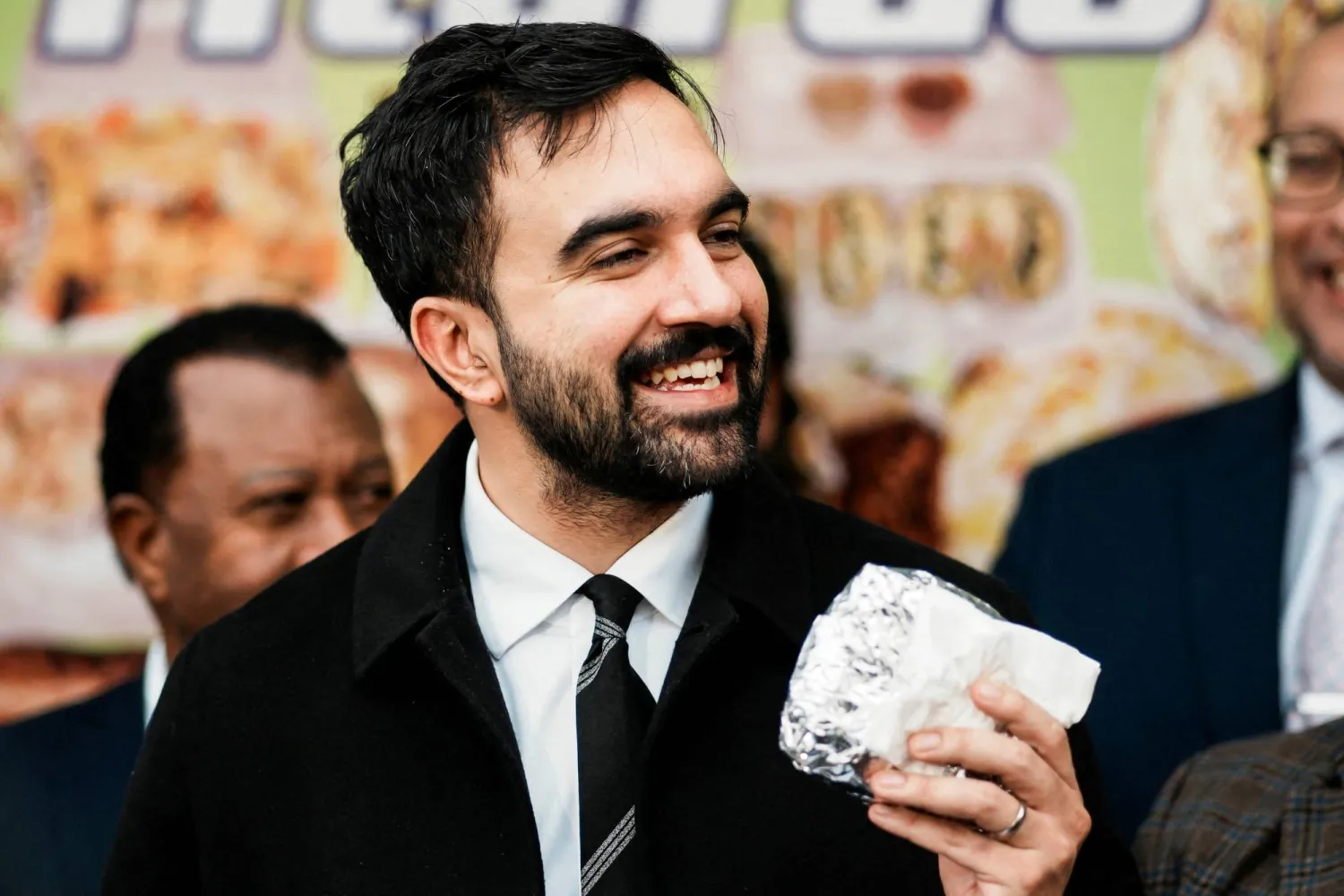 زهران ممداني يحمل شطيرة أثناء حديثه إلى وسائل الإعلام في ضاحية برونكس بمدينة نيويورك يوم 29 أكتوبر (رويترز)