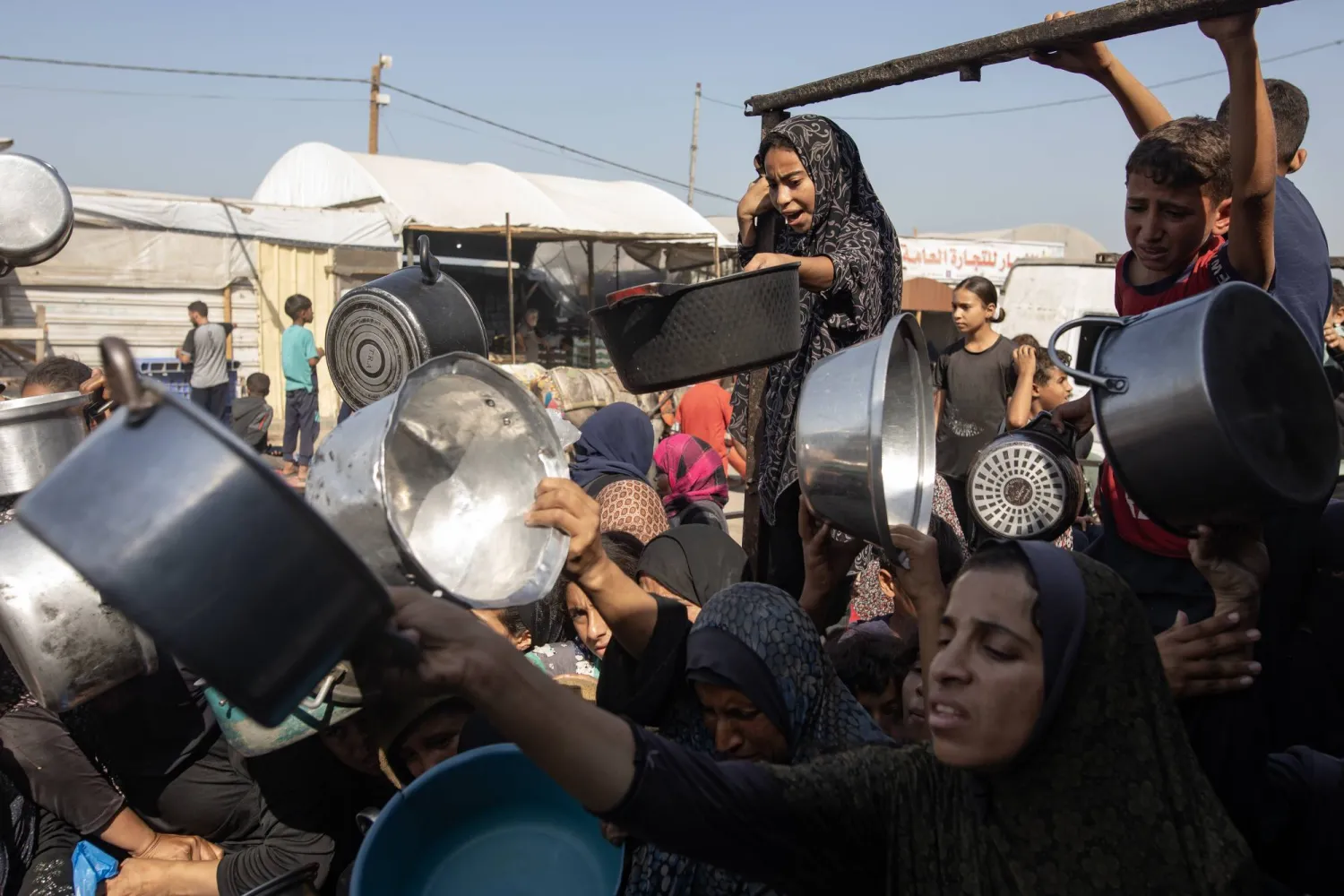 نازحون فلسطينيون يحاولون الحصول على وجبة طعام في مطبخ خيري بخان يونس جنوب قطاع غزة الجمعة (إ. ب. أ)