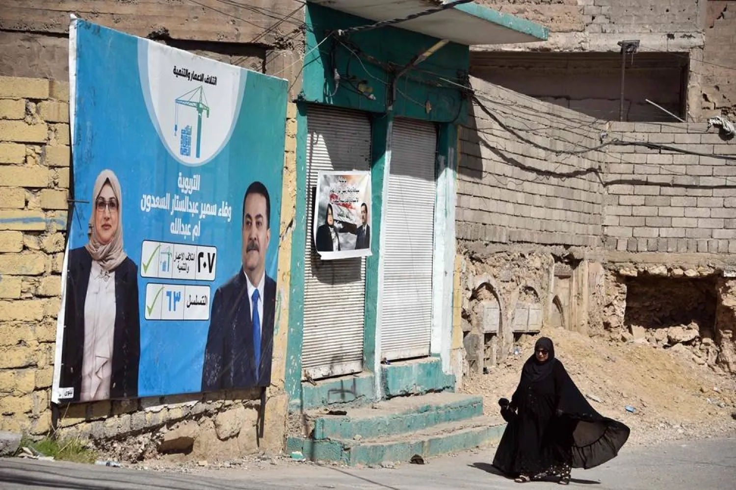 A woman walks past a banner depicting political candidates from a rival bloc, competing for a seat in the Iraqi parliament, days before the parliamentary elections, in Old Mosul, northern Iraq, on October 28, 2025. (EPA)