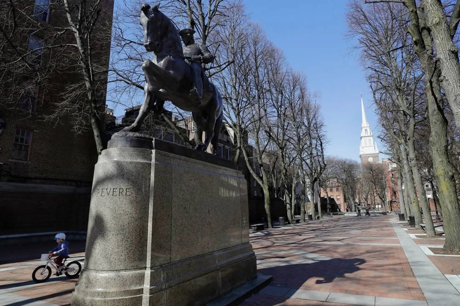 A child rides a bicycle, left, near a statue of Paul Revere in Boston's North End neighborhood on March 15, 2020. (AP)