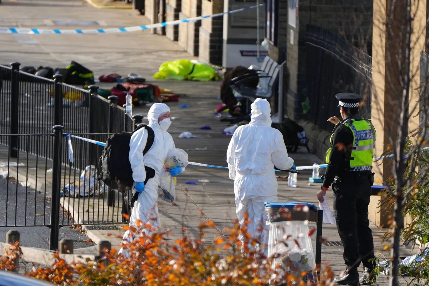 محققو الطب الشرعي يسيرون أمام المنطقة التي ترك فيها المسافرون أمتعتهم بعد طعن جماعي في قطار متجه إلى لندن في هانتينغدون بإنجلترا (أ.ب)