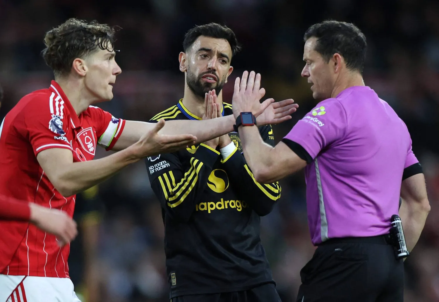 لاعب نوتنغهام رايان ييتس ولاعب يونايتد برونو فيرنانديز يحتجان على الحكم دارين إنغلاند (أ.ف.ب)