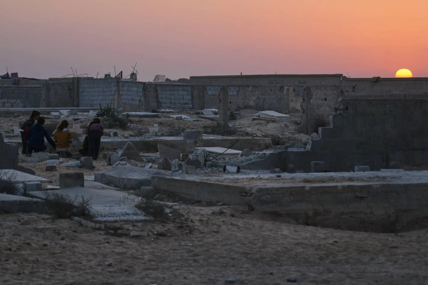 Palestinian children stand at a cemetery in Khan Younis, where a makeshift tent camp for displaced people was set up, as the sun sets in the southern Gaza Strip, Friday, Oct. 31, 2025. (AP Photo/Abdel Kareem Hana)