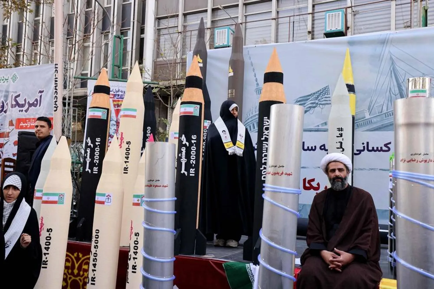People sit and others stand next to models missiles and nuclear enrichment centrifuge during a rally outside the former US embassy in Tehran as Iranians mark the 46th anniversary of the start of the Iran hostage crisis, on November 4, 2025. (AFP)